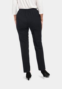 Zwarte, elastische broek met een elastische tailleband, taps toelopende broekspijpen, gladde textuur en een eenvoudige, klassieke uitstraling, gecombineerd met zwarte hakken.