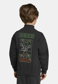 Felpa nera con colletto alto, con grafica verde e arancione di Topolino Disney sul retro e testo "ADIDAS 1949". Vita elasticizzata.