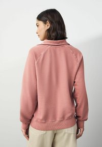 Różowy sweter z wysokim kołnierzem, ściągaczami na rękawach i u dołu, charakteryzujący się miękką teksturą. Widok z tyłu pokazuje zaokrąglone ramiona i czyste linie.