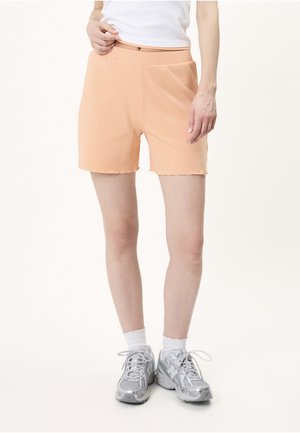 Person iført ferskenfarvede ribstrikkede shorts, hvide korte sokker, sølvfarvede sneakers og en hvid cropped top vist fra taljen til fødderne.
