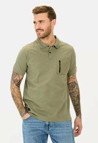 Olijfgroene polo-das gemaakt van lichtgewicht stof, met een kraag, een ritsborstas en korte mouwen.