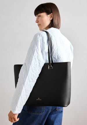 Borsa tote in pelle nera con texture a ciottoli, hardware in argento e un accento con logo. Indossata a spalla su uno sfondo chiaro.