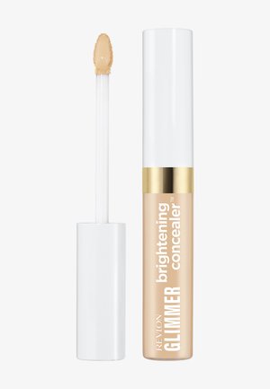 Correcteur illuminateur Revlon Glimmer avec capuchon blanc, bande dorée et liquide beige sur l'applicateur, sur fond blanc.