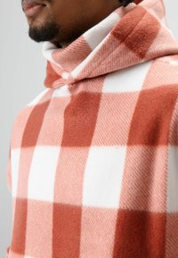 Rood-wit geruit fleece hooded sweatshirt met een hoge kraag. Zachte textuur en losse pasvorm, voorzien van een trekkoorddetail aan de capuchon.