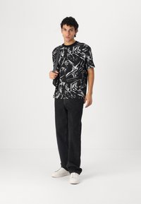Black and white patterned t-shirt with short sleeves, paired with black jeans and white sneakers. Subject holds a dark strap bag.