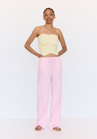 Un crop top jaune sans bretelles avec des rayures verticales, associé à un pantalon rose ample avec une taille élastique et un cordon de serrage. Sandales visibles.
