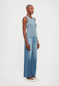 Light blue sleeveless top, paired with high-waisted, wide-leg faded denim jeans and pointed white heeled shoes. Simple, clean design.