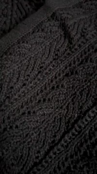 Țesătură tricotată gri închis cu modele complexe de diamante și cabluri, formând o suprafață texturată și confortabilă.