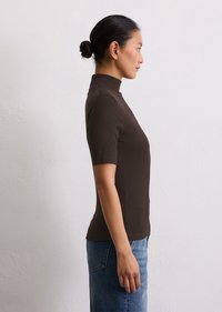 Haut en maille côtelée marron à col roulé, à manches courtes, au design ajusté et à la texture douce, associé à un jean en denim bleu taille haute.