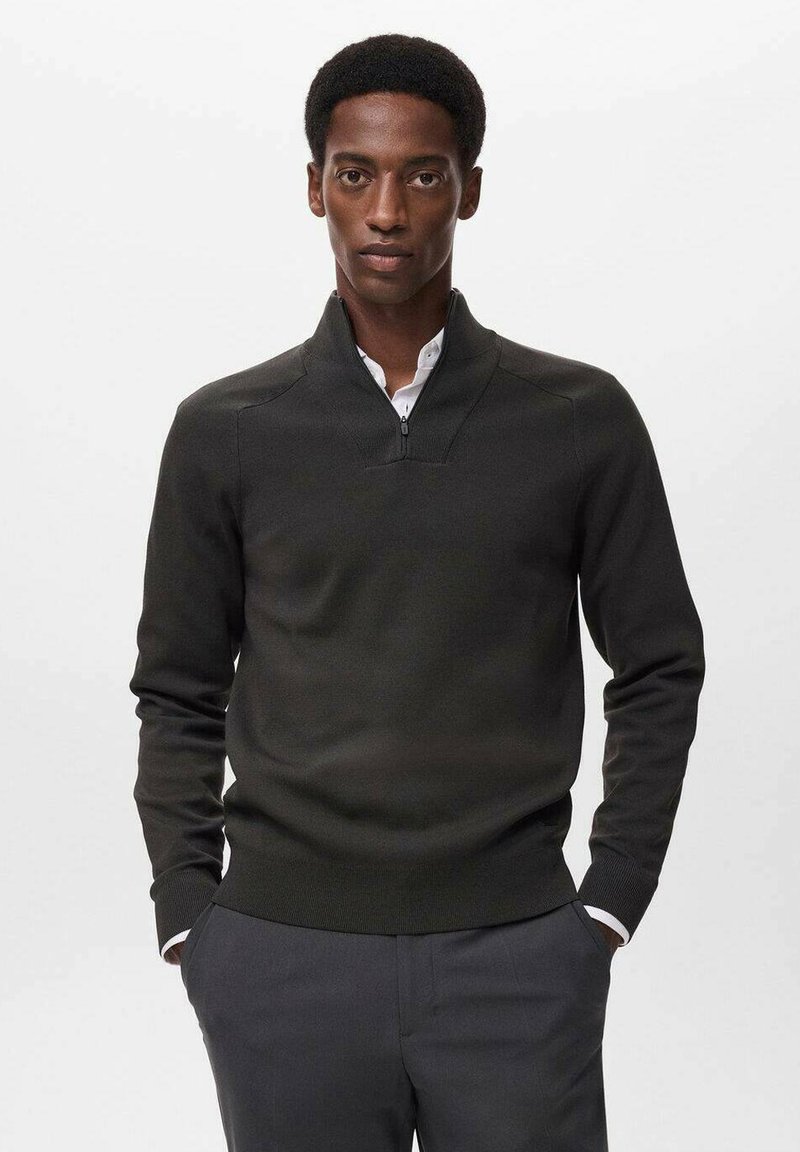 Mørkegrøn strikket sweater med lynlås krave, med en tætsiddende pasform og ribbede manchetter, parret med en hvid skjorte med krave under.