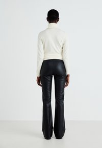 White turtleneck sweater with ribbed texture, paired with high-waisted, flared black faux leather pants, viewed from the back.