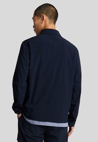 Giacca leggera blu navy con vestibilità dritta, colletto e maniche lunghe. Caratterizzata da un design minimal e una texture liscia.