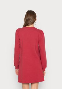 Bordeauxrotes Kleid mit langen Puffärmeln, rundem Ausschnitt und lockerem Schnitt. Aus weichem Stoff gefertigt, weist es minimale Nähte auf.