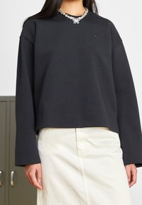 Black sweatshirt with a rounded neckline, featuring a decorative butterfly design and a cropped fit. Long sleeves and soft texture.