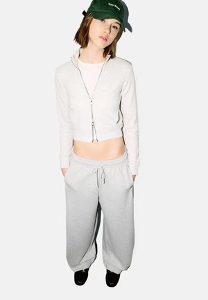 Hellgraue, kurze Zip-up Sweatshirt mit langen Ärmeln, kombiniert mit lockeren grauen Jogginghosen mit elastischem Bund und Taschen. Grüne Mütze.