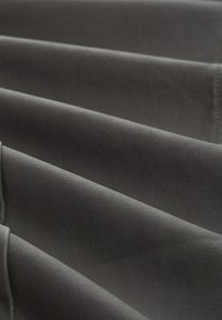 Tejido gris con una sutil trama texturizada, dispuesto en capas dobladas, que muestra superficies suaves y tonos suaves y apagados.