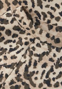 Kůže s leopardím vzorem v béžové barvě, která obsahuje mix černých a tmavě hnědých skvrn. Měkká textilie s mírným elastickým efektem, která obrysově zvýrazňuje výstřih a švy.