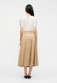 Λευκή κοντομάνικη μπλούζα με άνοιγμα στην πλάτη, σε συνδυασμό με μια πλισέ, μακριά μπεζ φούστα. Και τα δύο έχουν λείο ύφασμα. Μαύρα παπούτσια ολοκληρώνουν το σύνολο.