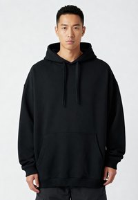 Felpa nera in cotone con cappuccio e tasca a marsupio, polsini e orlo a costine, caratterizzata da una vestibilità rilassata e lacci piatti.