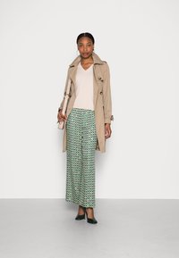 Beige trenčkot přes světlo barevný svetr, doplněný vzorovanými širokými kalhotami v tyrkysové a zelené barvě. Černé lodičky a malá taška outfit dotváří.