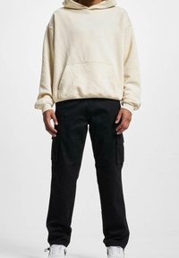 Krämfärgad bomullshuvtröja med en framficka, parat med svarta cargobyxor som har sidofickor. Vita sneakers fulländar outfitten.