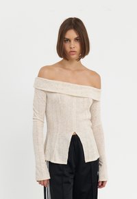 Off-shoulder topp i lys beige ribbet stoff med lange ermer, med en frontslitt og en teksturert, lett utslått design.