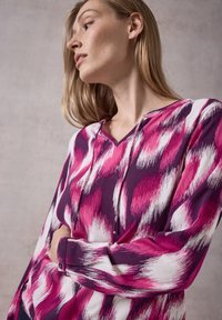 Blusa a maniche lunghe con motivo multicolore rosa e bianco, caratterizzata da scollatura a V e dettagli con bottoni ai polsini, realizzata in tessuto liscio.