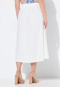 Witte, knie-lange rok met een gerimpelde taille en zijsploezen. Glad stof met een vloeiende uitstraling. G gedragen met huidkleurige blokhak sandalen.