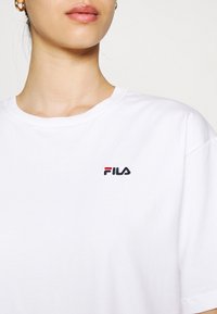 T-shirt bianco in cotone con un piccolo logo Fila ricamato in nero e rosso sulla parte sinistra del petto. Design classico a collo rotondo.