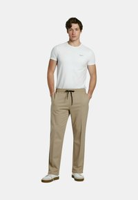 Beige broek met losse pasvorm, trekkoord in de taille en zijzakken, gecombineerd met een wit eenvoudig T-shirt met korte mouwen en witte sneakers.