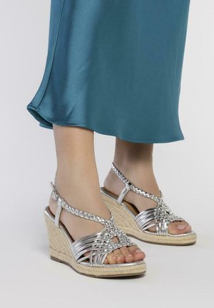 Sandalias de cuña plateadas con tiras trenzadas, punta abierta y detalles de yute tejido en la cuña. Textura suave y diseño elegante.