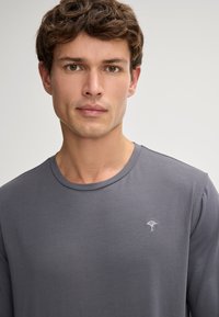 Grå lange ærmer T-shirt lavet af glat stof med rund halsudskæring. Har et lille broderet logo på venstre brystområde.