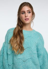 Hellblaues, übergroßes Sweatshirt mit einem strukturierten Strickmuster, das über einen runden Ausschnitt und überschnittene Schultern verfügt und eine weiche, flauschige Oberfläche zeigt.
