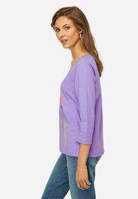 Camicia lavanda a maniche tre quarti con design grafico sul davanti, realizzata in tessuto morbido, con una vestibilità ampia e scollo rotondo.