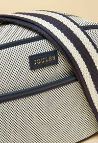 Sac en toile à petit motif à carreaux noir et blanc, bordure marine, bandoulière rayée marine et crème, et étiquette logo "Joules" dorée.