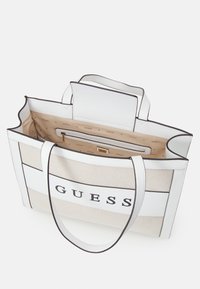 Biała i beżowa torba na ramię z czarnymi akcentami, wykonana z teksturowanej tkaniny, z logo nadrukowanym z przodu oraz przestronnym wnętrzem z wzorzystą podszewką.