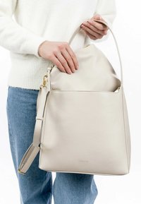 Light beige leather handbag with a wide opening, single top handle, adjustable shoulder strap, and a smooth texture. Minimalist design.