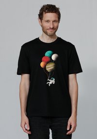 T-shirt en coton noir avec un graphique coloré de planètes et un astronaute tenant des cordes de ballons. Manches courtes et coupe standard.
