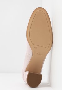 Chaussure à talon haut en daim rose blush avec un bout carré et une semelle en caoutchouc marron clair, arborant un logo de marque et un détail texturé sur le talon.
