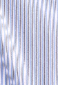 Gros plan sur un tissu bleu clair avec de fines rayures verticales bleu marine, blanches et marron, montrant la texture et un motif finement tissé.