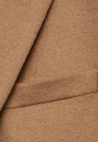 Smeđi vune s mekanom, teksturiranom površinom. Ima čist, moderan dizajn s suptilnim detaljem džepa.