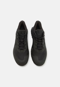 Scarpe sportive nere con tomaia in rete, superfici testurizzate, lacci tondi e una suola in gomma robusta con un disegno a tasselli.