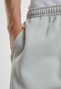 Helle graue Sweatpants bestehen aus weichem Stoff, haben einen elastischen Bund und seitliche Taschen. Die Textur ist glatt und der Schnitt ist locker um die Hüften.