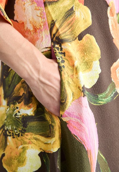 Blomsterdekket stoff med store oransje, rosa og gule blomster på en brun bakgrunn; inkluderer en sidelomme og strukturert overflate.