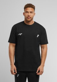 Sort bomulds T-shirt med korte ærmer, der har et hvidt logo på venstre bryst og en hvid detalje nær skulderen.