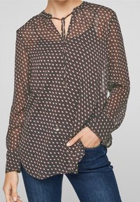 Blusa nera trasparente con un design a motivo che presenta forme rosse e bianche, scollatura a cravatta e dettagli in bottone sulla parte anteriore.