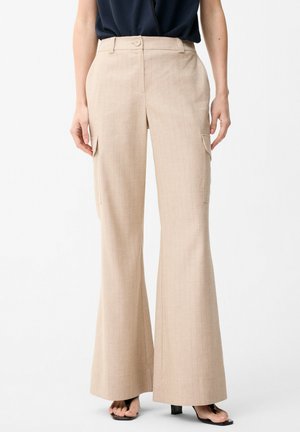 Beige hoch taillierte, weit geschnittene Hose mit seitlichen Klappentaschen, kombiniert mit schwarzen offenen High Heels und einem in den Bund gesteckten schwarzen Top.