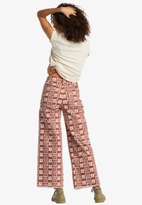 Wide-leg pants in red with a white floral pattern, made from lightweight fabric, featuring a high waist and raw hem details.