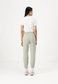 Lichtgroene joggingbroek met elastische tailleband en boorden, gedragen met een wit T-shirt en lichtroze sneakers, weergegeven vanaf de achterkant.