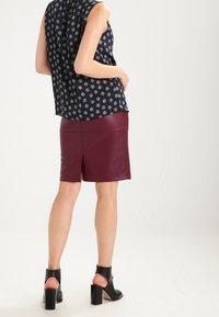 Námořnický modrý květinový top s krátkými rukávy, doplněný burgundy koženou tužkovou sukní s rozparkem vzadu. Černé sandály na blokovém podpatku.